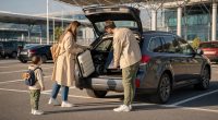 Familie care pregătește bagajele lângă o mașină închiriată, în apropierea unui aeroport